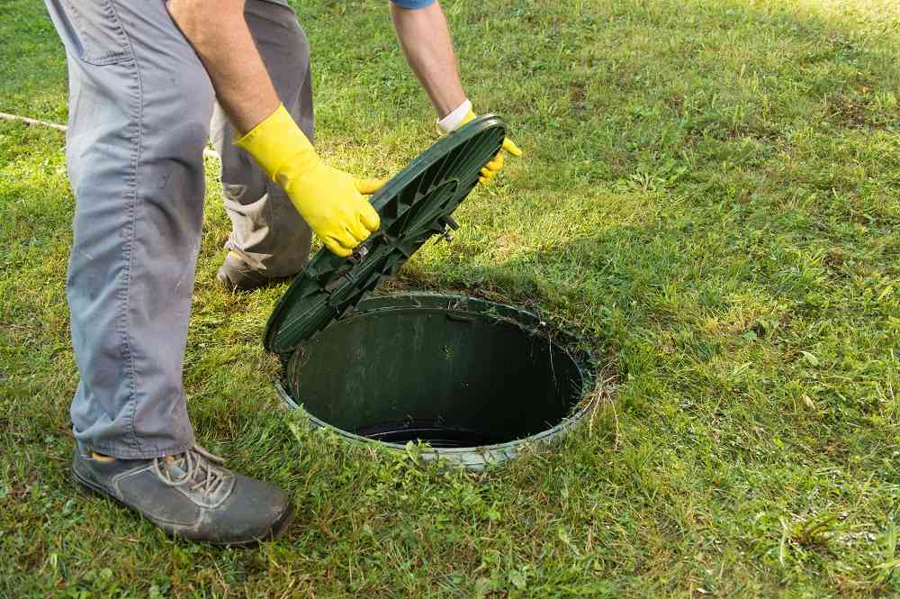 Muž v rukavicích zvedá víko septiku.